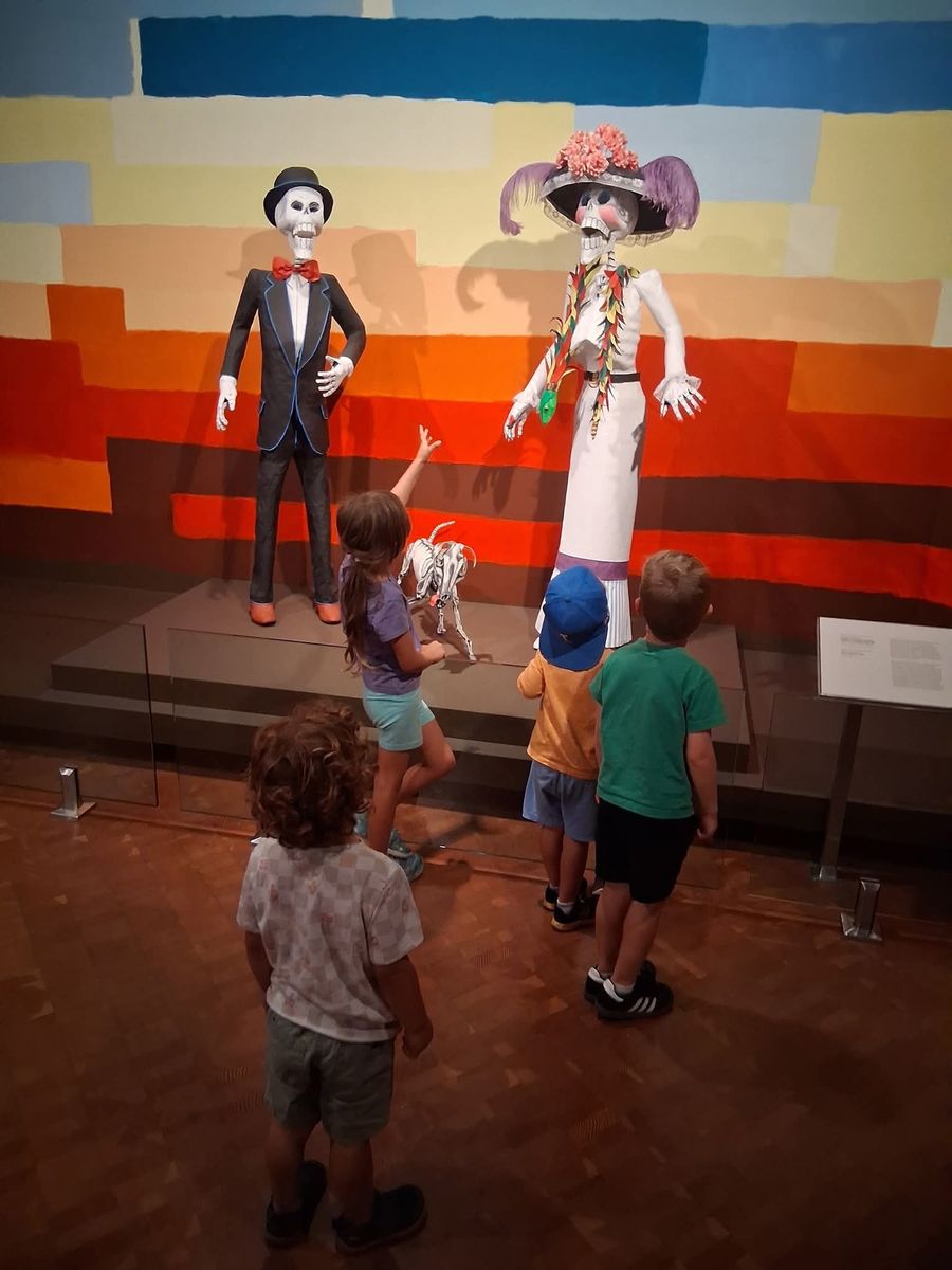 Children looking up at two towering Day of the Dead skeleton figures in a museum